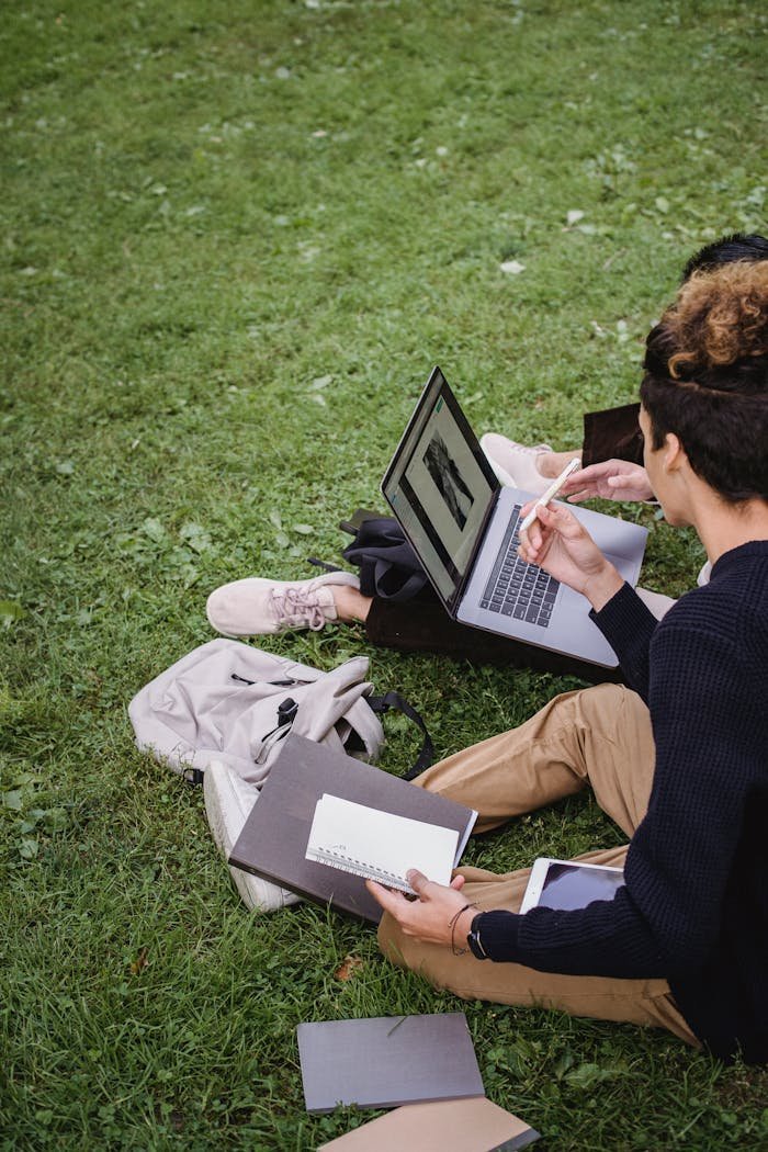our-mission Two students study together on a laptop outdoors, surrounded by books.