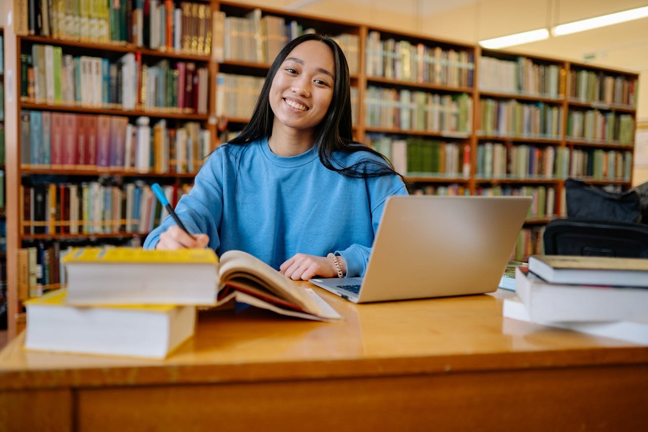 portfolio-04 Smiling student studying in a library with books and laptop, showcasing education and focus.
